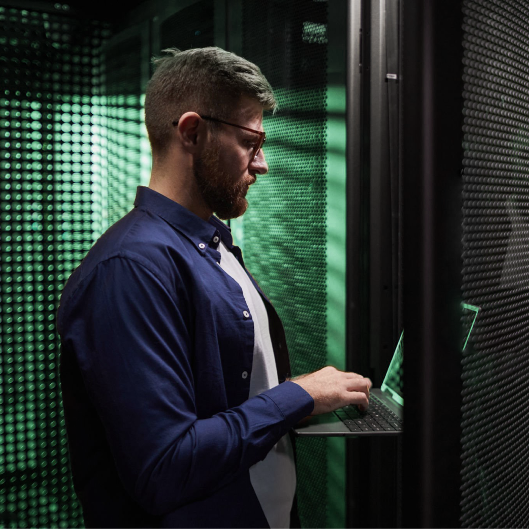 Service & Lifecycle-Support von Cyrus für Industriegeräte Administrator arbeitet mit Laptop im Serverraum – Wartung und Optimierung moderner Datencenter-Infrastruktur